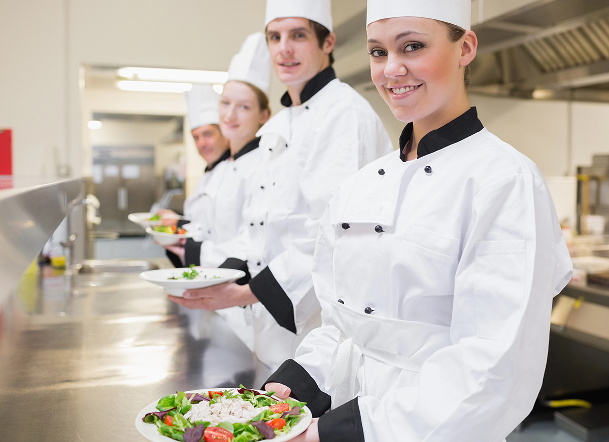Junge Köche am Arbeitsplatz mit Salattellern in den Händen