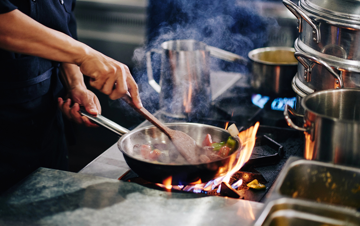 Koch rührt Gemüse in einer Pfanne über Herdflammen